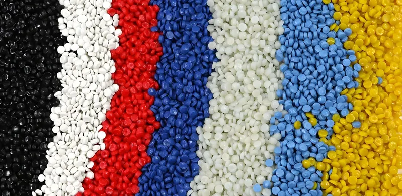 Various colors of plastic pellets arranged in vertical strips, including black, white, red, blue, light green, light blue, and yellow