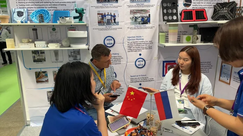 Group of people having a discussion at a trade show booth with Chinese and Russian flags on the table.