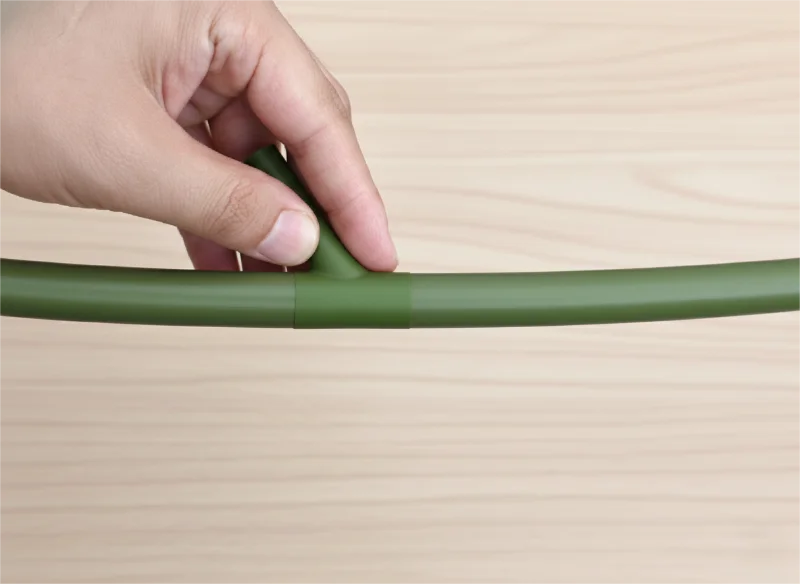 Close-up of a hand holding a green connector aligning bamboo pieces on a wooden surface.