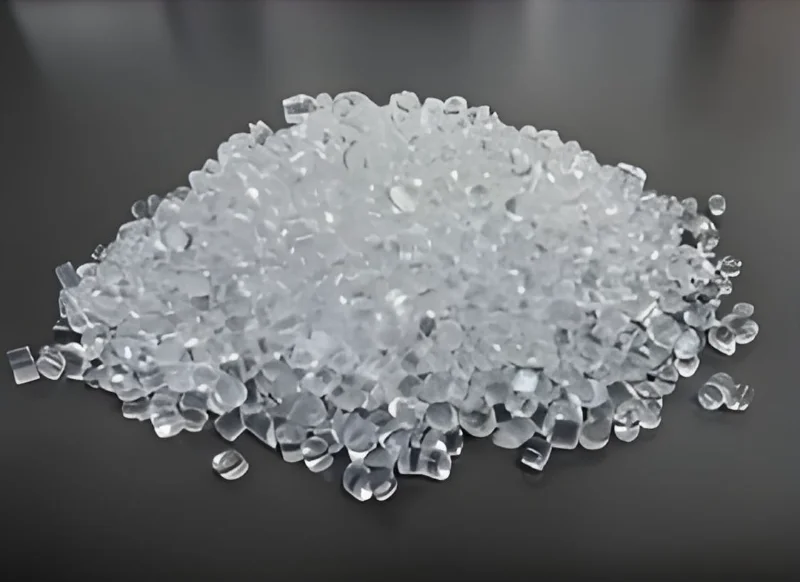 A pile of clear plastic pellets scattered across a dark surface, used as raw material in manufacturing.