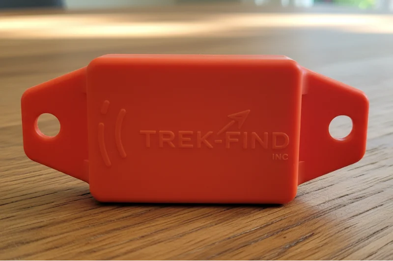 Orange Trek-Find GPS tracker with attachment holes on a wooden surface.